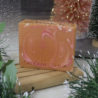 Orange Bar of soap with red and white swirls sitting on a woodensoap rack, surrounded by decorative elements.