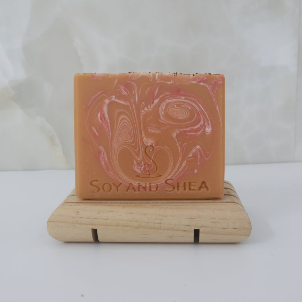 Orange bar of soap with pink and white swirls on a wooden stand against a white background