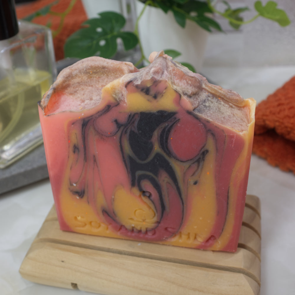 Marbled Orange, yellow and black soap bar on a wooden soap rack with a blurred bathroom background