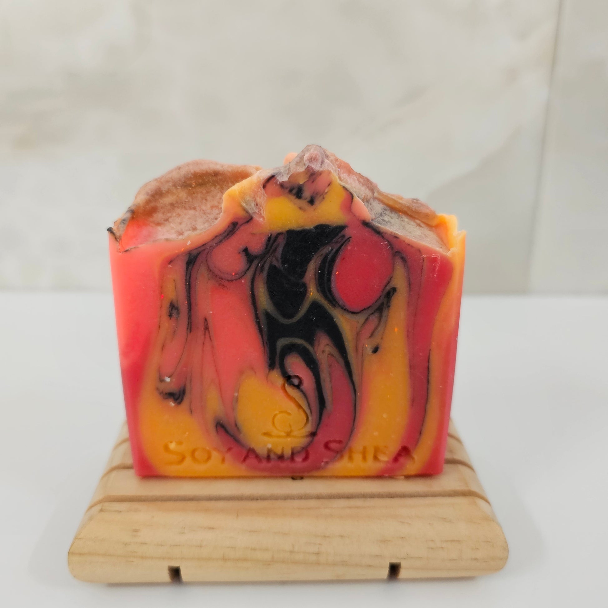 A soap bar with bright orange, yellow and black swirls sit on a wood block surrounded by marble tile