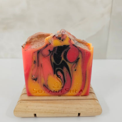 A soap bar with bright orange, yellow and black swirls sit on a wood block surrounded by marble tile