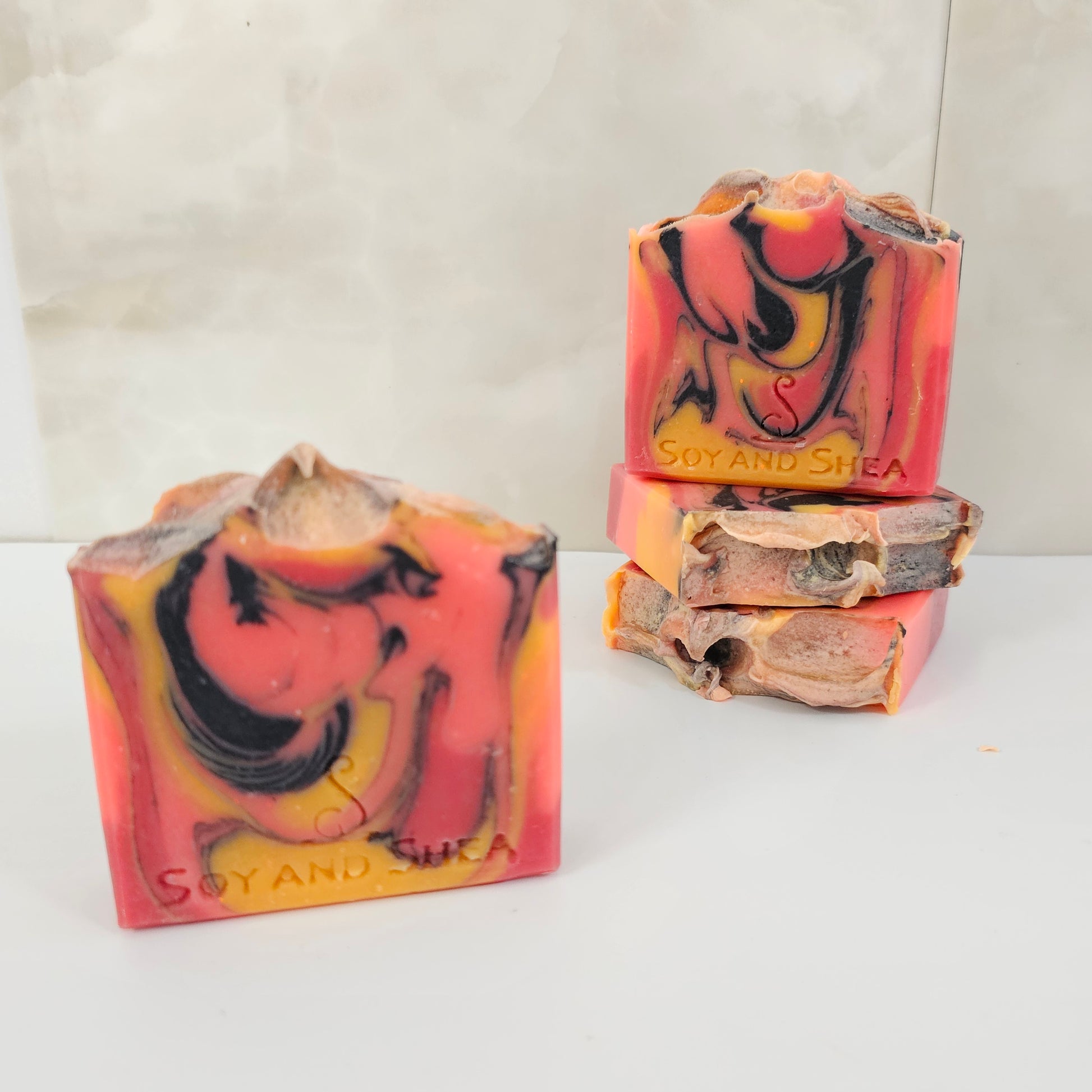 A selection of four bright orange soap bars with yellow and black swirls with on a marble tile.  Two soaps are laying down showing a textured top while the other two stand on their base showing two different designs