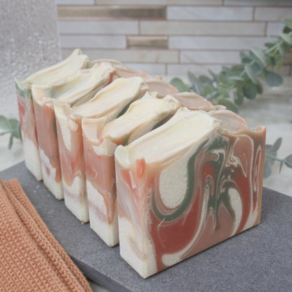 Marbled soap bars on a gray surface with a blurred background.  The soaps are lined up one in front of the other.  Only the front soap shows a marble design of orange, red, white and green