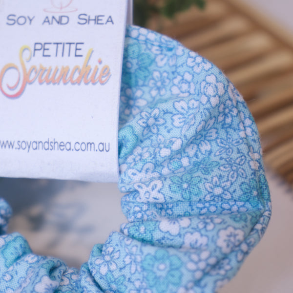 A close up of the Forget-me-not scrunchie fabric showing small white and teal floweres scattered over a pale blue fabric.  