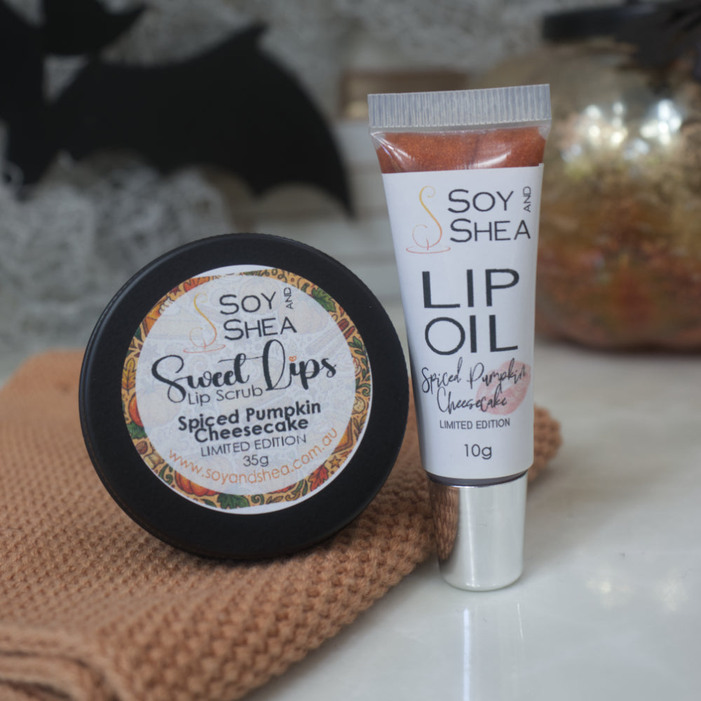 A tin of Sweet Lips lip scrub and tube of lip oil in a warm pumpkin spice flavor, displayed on a white surface with a brown textured cloth.