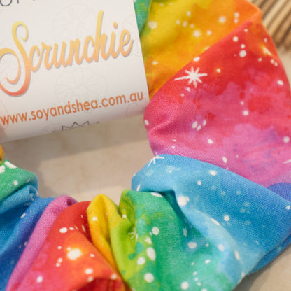 A close up photo of the fabric on the Rainbow scrunchie.  It features rows of bright rainbow colours with a watercolour effect covered in white dots and stars.