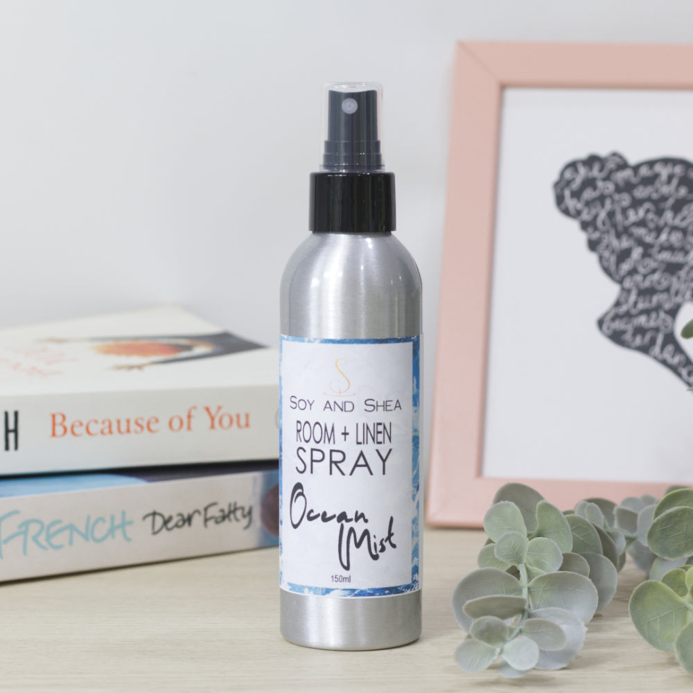 Room and linen spray bottle labeled 'Ocean Mist' on a surface with books and a framed picture in the background.