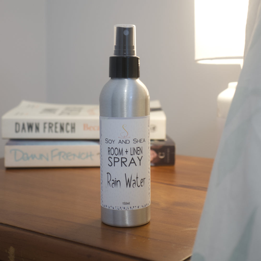 Room and linen spray bottle labeled 'Rain Water' on a wooden surface with books in the background.