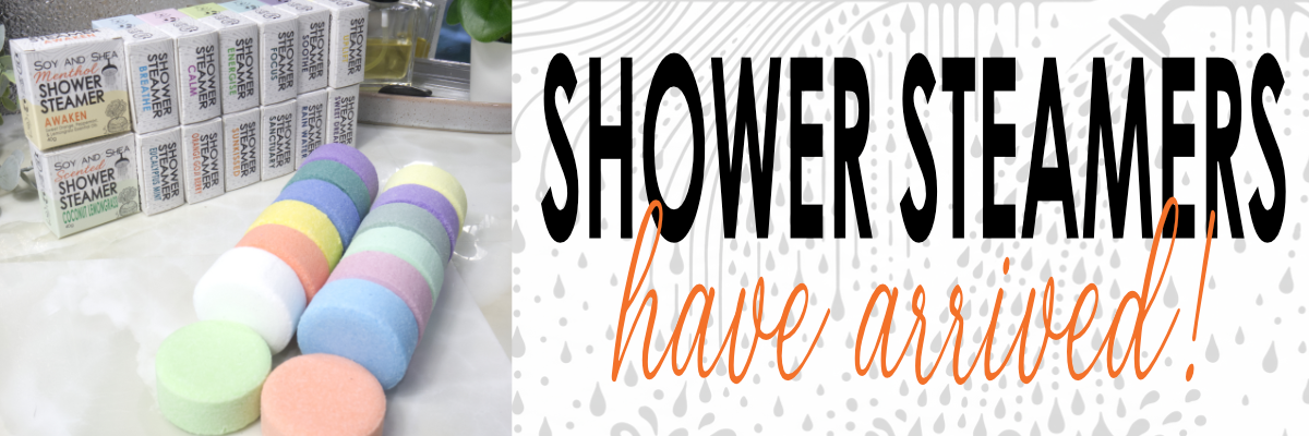 A promotional banner for Shower Steamers, featuring a collage of colorful round steamers and a row of branded product boxes on the left, next to large text reading 'SHOWER STEAMERS have arrived!' on the right.
