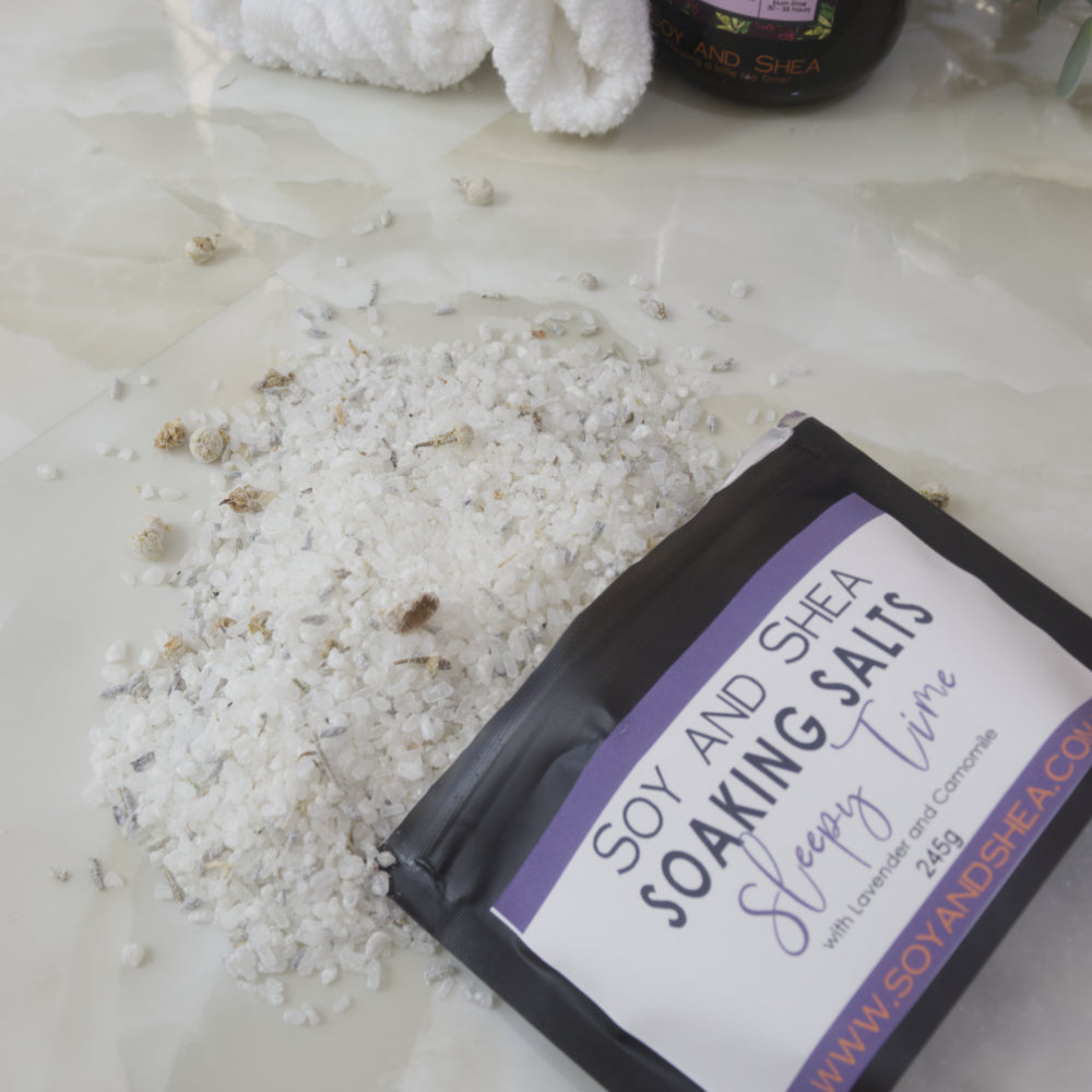 A black pouch of Soy and Shea Soaking Salts with a purple label spilled across a marble bench