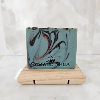 A green soap with black and gold swirls sits on a wooden stand in front of marble tiles
