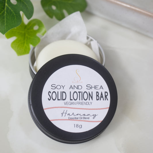 A small black round tin sits on a marble surface with a greenery to the back left of the overhead shot.  The lid of the tn has been removed and rests on the side revealing a solid white lotion nestled in some paper inside the tin