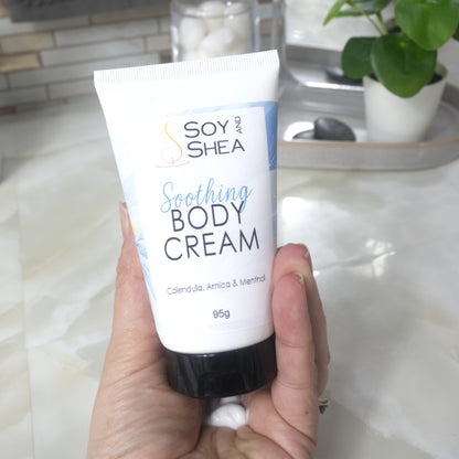 A hand holds a white tube with black cap labelled as Soothing Body Cream with calendula, Arnica and menthol.  In the palm of the hand is a dollop of white cream that has been squeezed out of tube. 