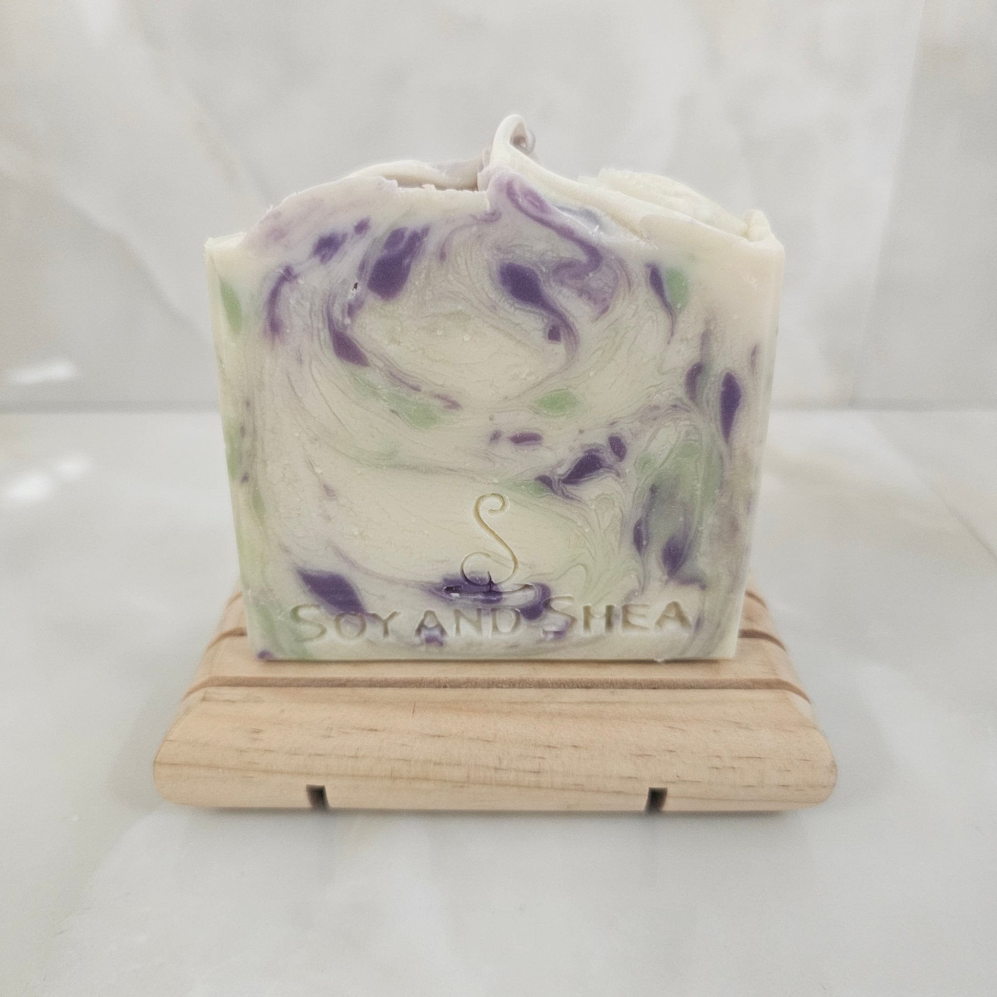White Bar of soap with purple and green swirls on a wooden soap dish against a white background