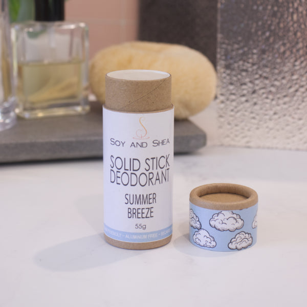 A cardboard tube labelled SOLID STICK DEODORANT stands upright on a bathroom counter top with a blurred background.  The lid of the tube sits to the left revealing the cream balm in the tube