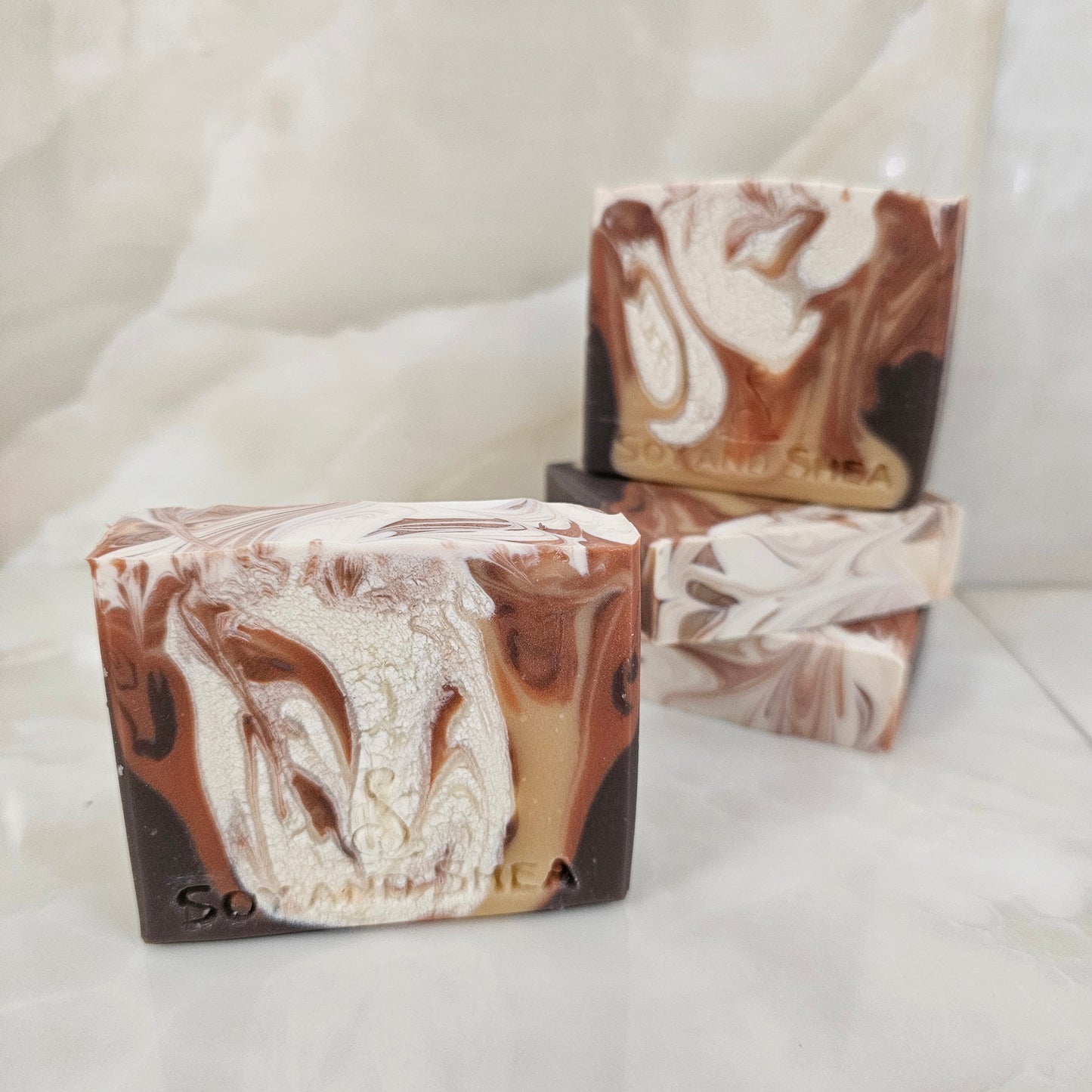 A selection of marbled soap bars with brown and white swirled pattern on a white background