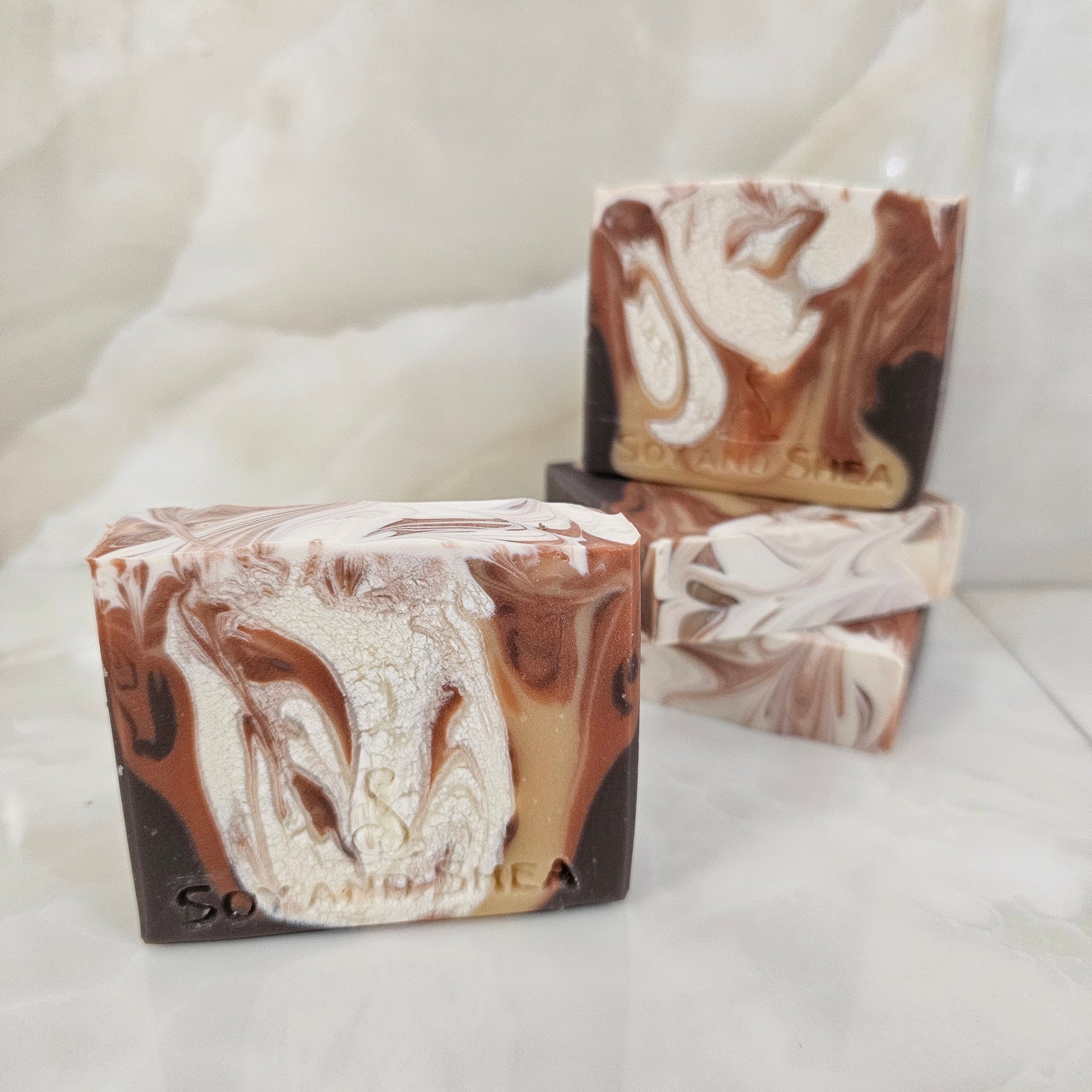 A selection of marbled soap bars with brown and white swirled pattern on a white background