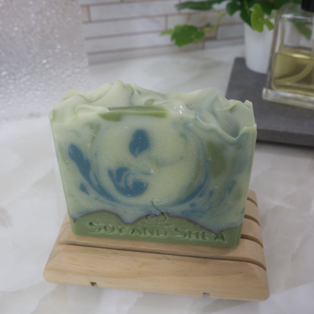 Pale green soap bar with dark green swirls on a wooden stand against a white background