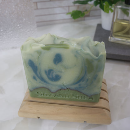 Pale green soap bar with dark green swirls on a wooden stand against a white background