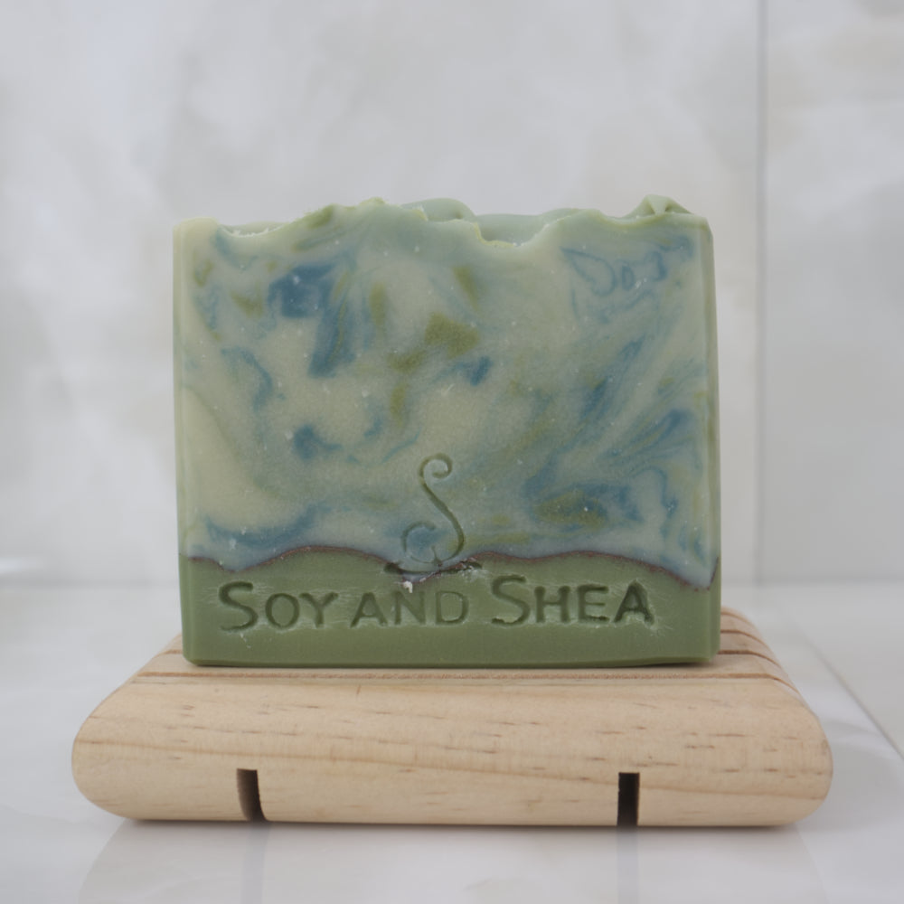Pale green soap bar with dark green swirls on a wooden stand against a white background