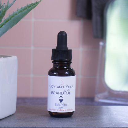 A brown bottle with white label and black dropper lid stands on stone surface next to a pot with green leaves against a blurred tiled background.  The label reads BEARD AND MO OIL and shows the image of a man with bead and moustache.