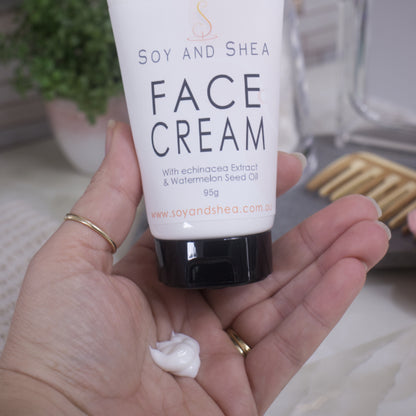 A hand is holding a tube of Soy and Shea Face Cream with a small amount of white cream on the palm. 