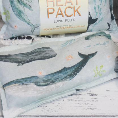 A Whales Mini Heat Pack rests on white side with another packaged Mini Heat Pack behind.  The image focuses on the design of the fabric which is pale blue with a variety of whale species