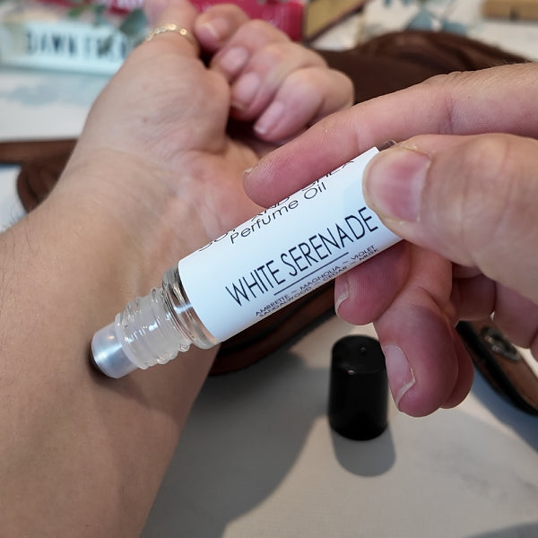 A person is applying a roller bottle of perfume oil labelled WHITE SERENITY to the other wrist. 