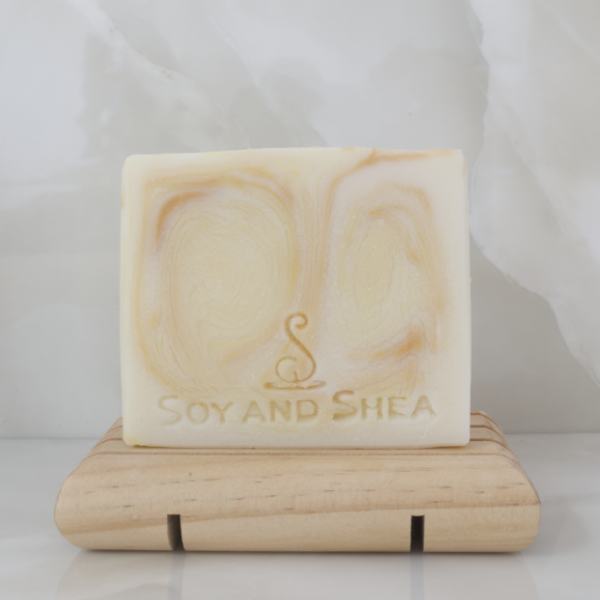 A white soap with golden swirls sits on a wooden soap dish against a marble tile background