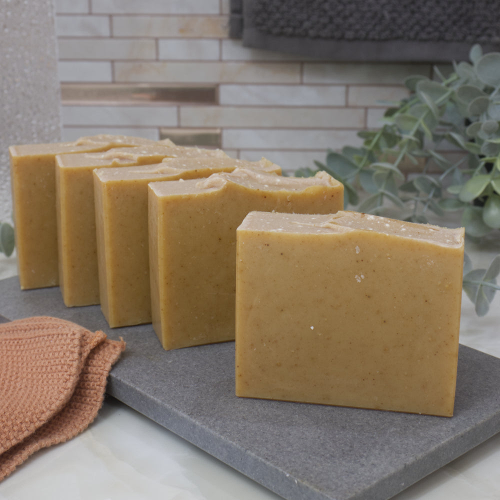Row of yellow soap bars on a gray surface with a tiled wall and plant in the background