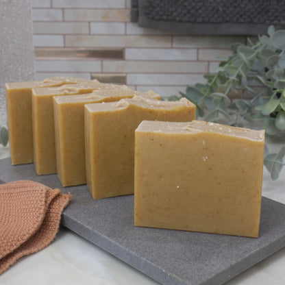 Row of yellow soap bars on a gray surface with a tiled wall and plant in the background