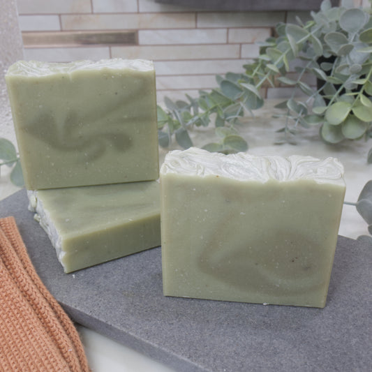 Three pale green bars of soap  with dark green swirls on a gray surface with a plant in the background