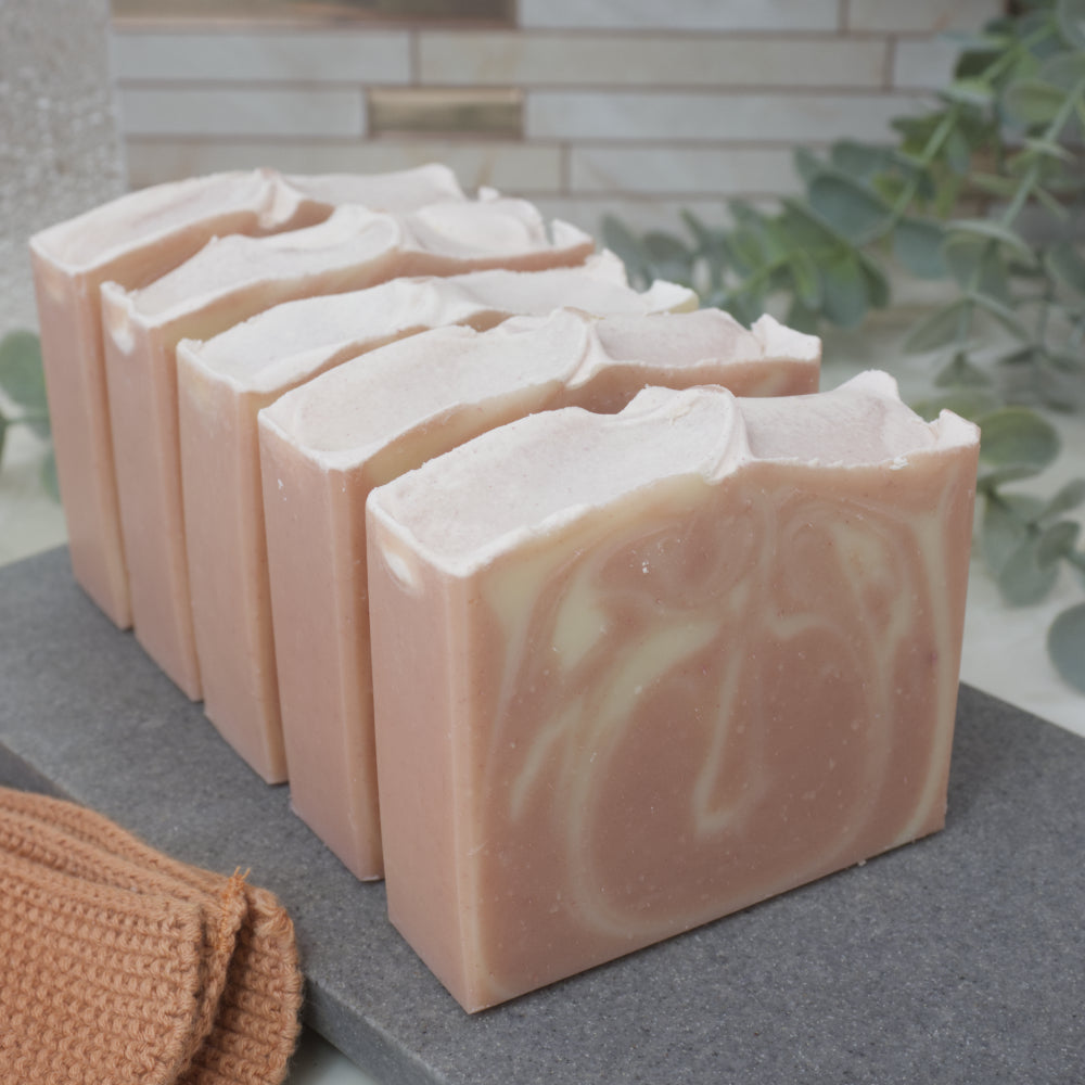 Row of soap bars with a pink and white marbled design on a gray surface, with a blurred background.