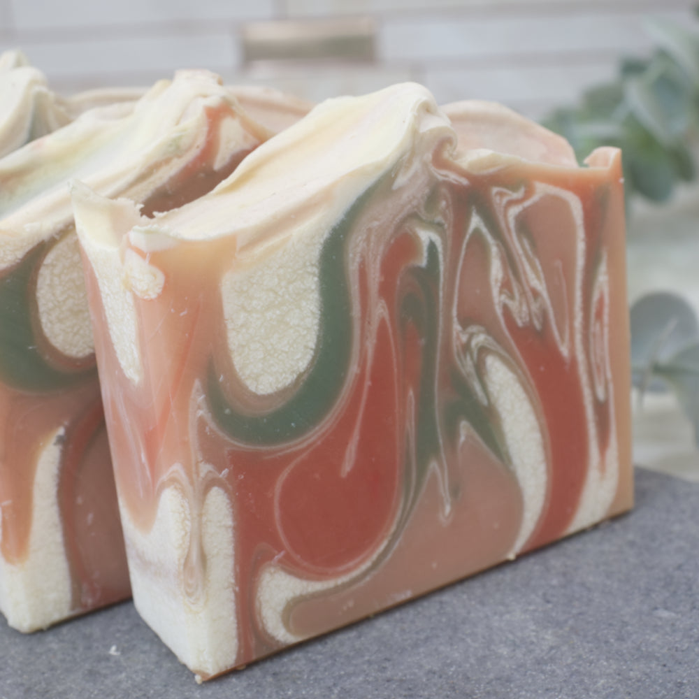A close up of a marbled soap bars with orange red, green, and white swirled colors on a gray surface.