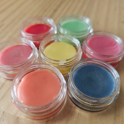 Set of colorful lip balms in clear containers on a wooden surface