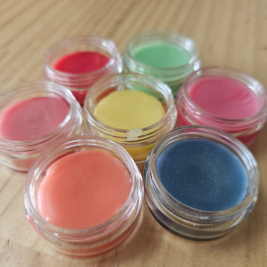 Set of colorful lip balms in clear containers on a wooden surface
