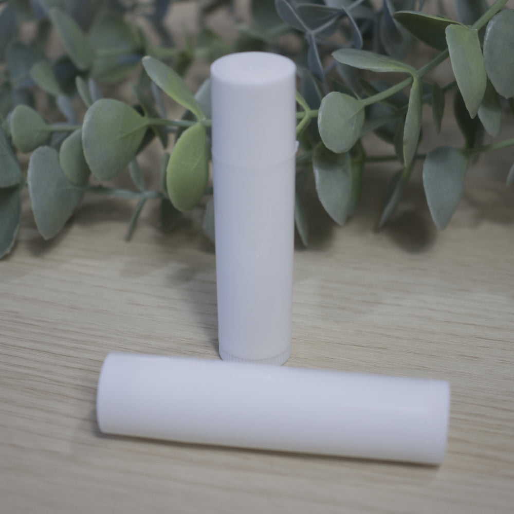 Two white cylindrical tubes sit on a wooden surface with green leaves in the background