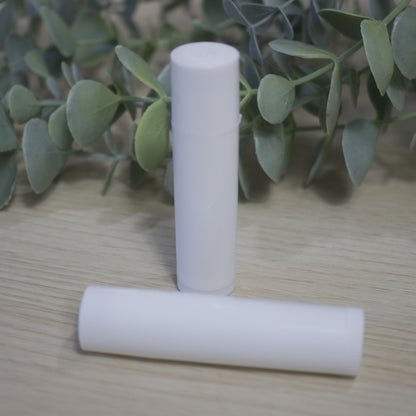 Two white cylindrical tubes sit on a wooden surface with green leaves in the background