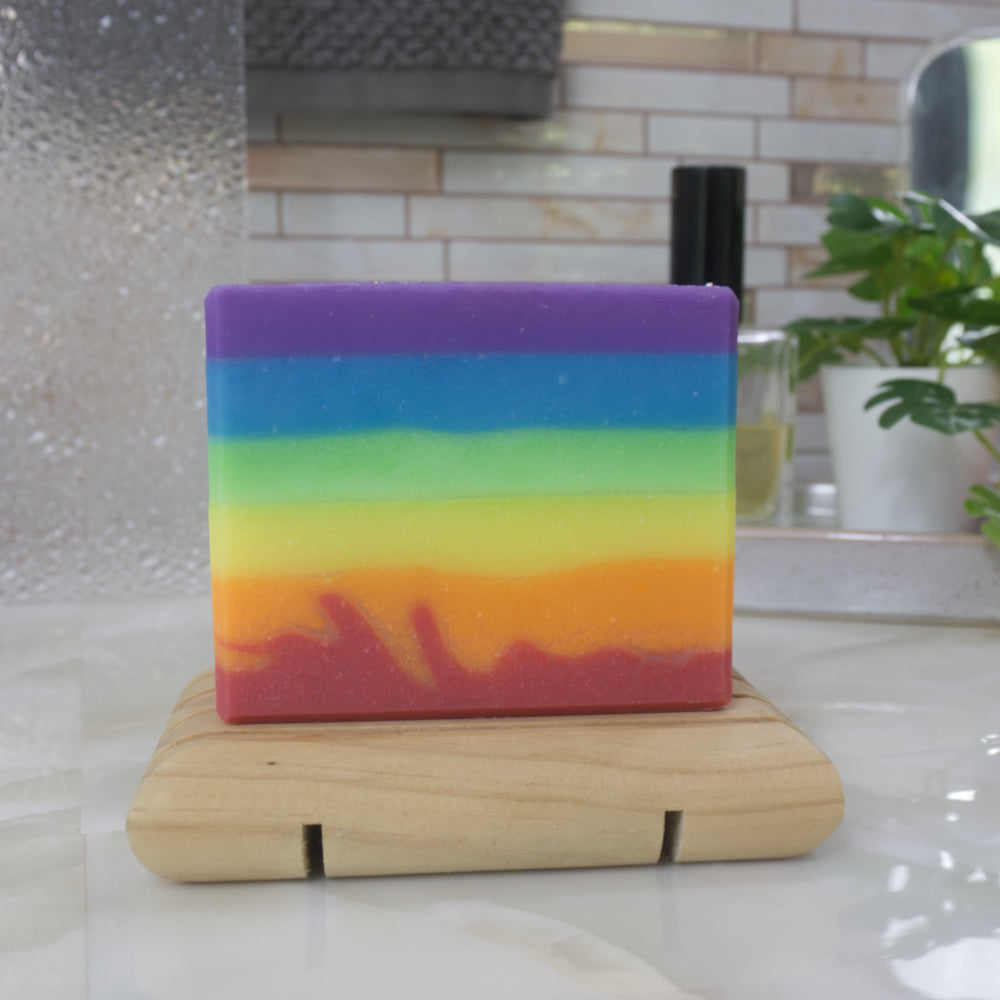A soap with rainbow-colored  layers which are uneven on a wooden stand with a blurred bathroom background