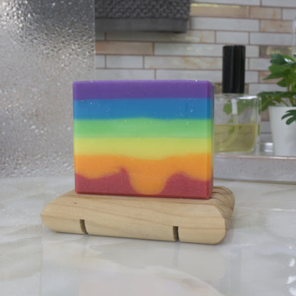 A soap with rainbow-colored  layers which are uneven on a wooden stand with a blurred bathroom background