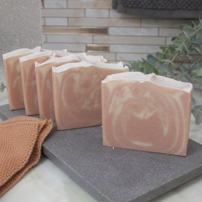 Pink and white swirled soap bars on a gray stone surface with a brown towel and greenery in the background.