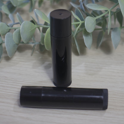 Two black cylindrical tubes sit on a light wooden surface with green leaves in the background